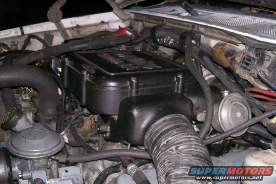 Engine bay with black intake manifold and hoses. Supermotors.net logo visible