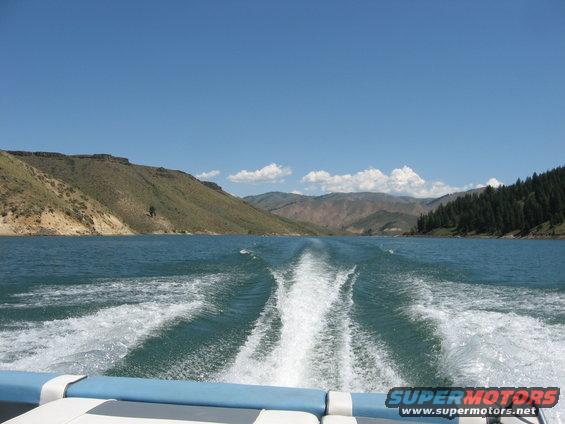 Wake from a boat on a lake with mountains and trees in the background. Supermotors.net logo visible