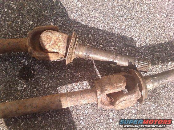 Two rusty driveshafts with universal joints, lying on asphalt