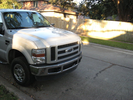 Silver Ford Super Duty truck parked on street, front quarter view. The grille has 'SUPER DUTY' text above the Ford emblem