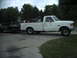 1987 Ford F-250 - A white 1987 Ford F-250 pickup truck is shown from the side, towing a trailer filled with various items.