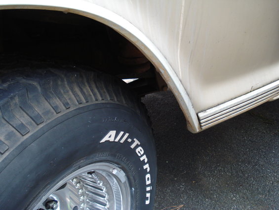 Cream-colored vehicle's rear wheel well and tire with "All-Terrain" text. Chrome rim visible