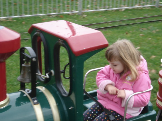 Little girl in pink jacket riding a toy train with a bell