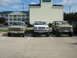 1993 Ford Bronco - Three lifted trucks, including a Ford Bronco and two F-Series models, are parked in a lot outside a hotel.