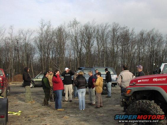 Group of people standing around several off-road vehicles in a wooded area