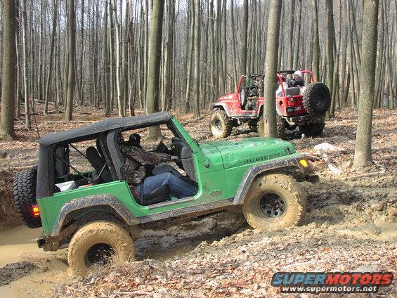 Green Jeep Wrangler and red Jeep Wrangler driving through mud in a forest