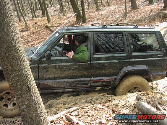 Green Jeep Cherokee XJ stuck in mud off-road, driver visible