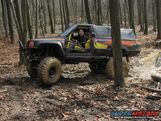 Modified off-road vehicle with large tires driving through mud and trees