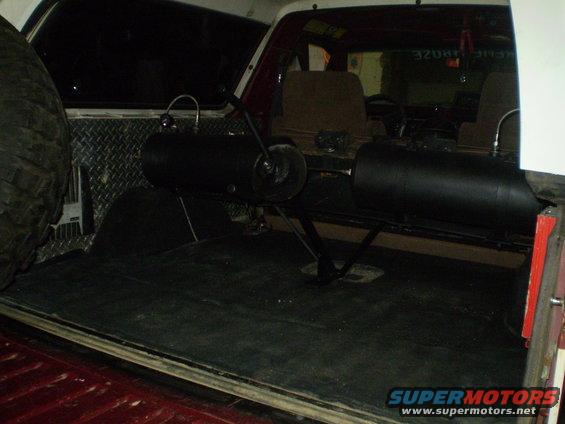 Interior cargo area of a red and white SUV, showing a spare tire, two black tanks, and diamond plate wall