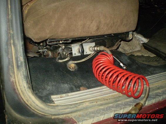 Close-up of a red coiled air hose connected to the underside of a vehicle seat
