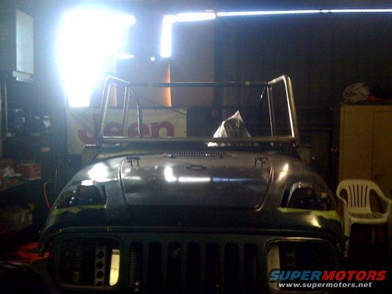 Front view of a 1994 Jeep YJ in a garage, undergoing some work. Roll cage is visible