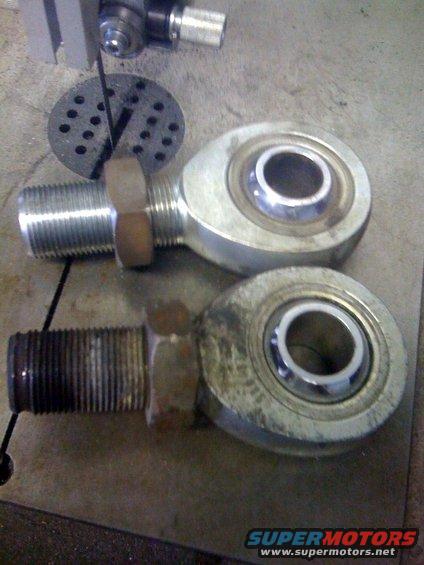 Two metal rod ends with threaded shafts and bearings on a concrete surface