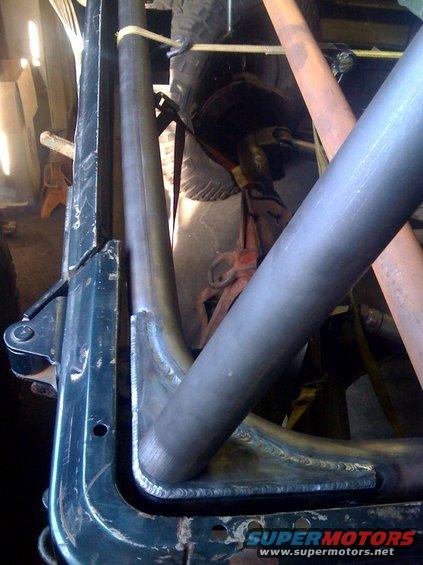 Close-up of custom roll cage tubing welded to a dark green vehicle frame, with a tire visible in the background