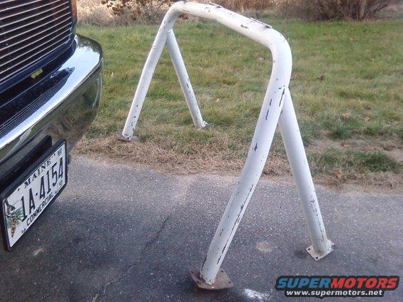 White metal roll bar attached to a vehicle's bumper area, with visible paint chips
