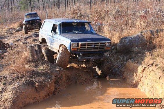 Blue Ford Bronco navigating a muddy off-road trail, with another SUV behind it