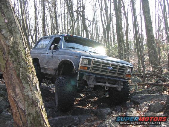 Dark gray Ford Bronco with lifted suspension and large tires driving over rocks in a forest
