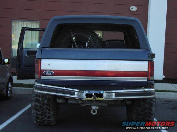 Rear view of a blue Ford Bronco with a spare tire inside, lifted suspension, and aftermarket bumper