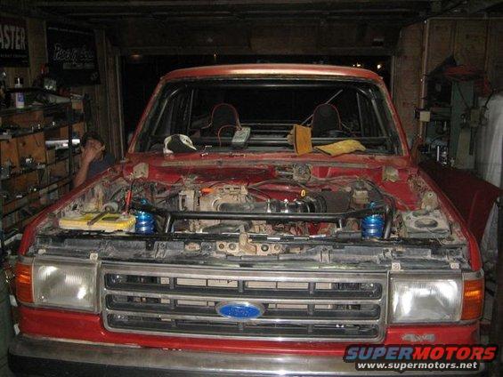 Red 1990 Ford Bronco with hood open, showing engine and roll cage. Front view
