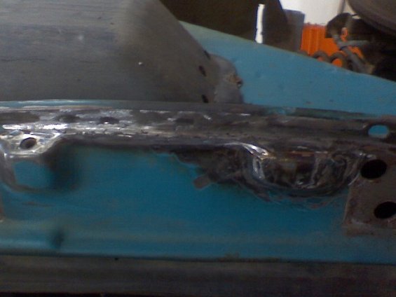 Close-up of a rusty, welded vehicle body panel with blue paint