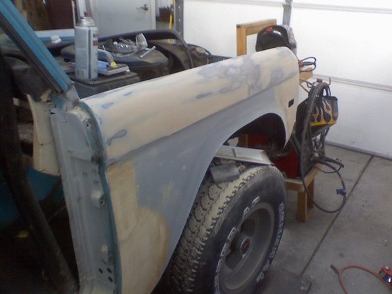 1972 Ford Bronco fender with primer and body filler, showing rust repair and a tire