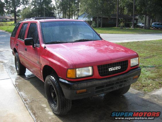 Red 1993 Isuzu Rodeo SUV parked on a wet driveway, front 3/4 view