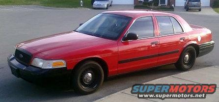 Red 2002 Ford Crown Victoria parked on a street. Another car is visible in the background