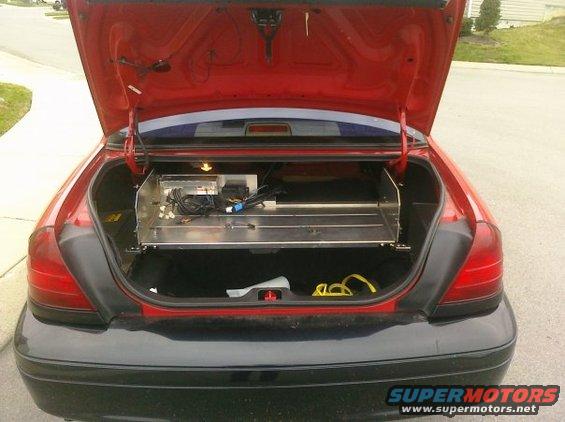 Rear of red car with trunk open, metal shelf with electronics inside