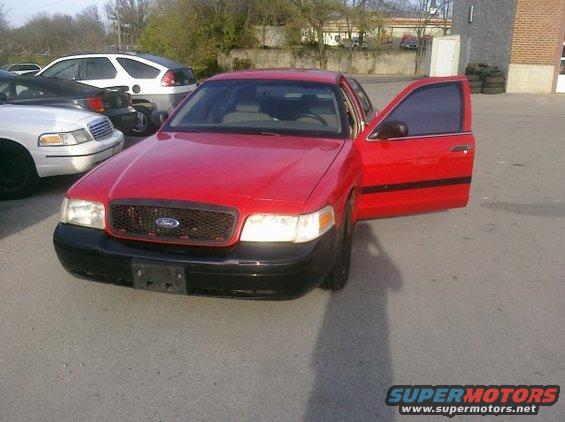 Red 2002 Ford Crown Victoria with driver's door open. Another Crown Victoria and a white SUV are parked nearby