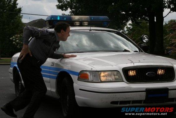 White 2000 Ford Crown Victoria police car, front view, with officer leaning on hood