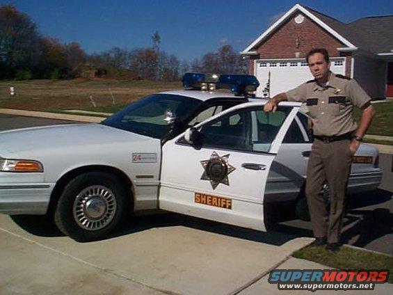 White 1997 Ford Crown Victoria police car with open driver's door, sheriff's star emblem, and "SHERIFF" text