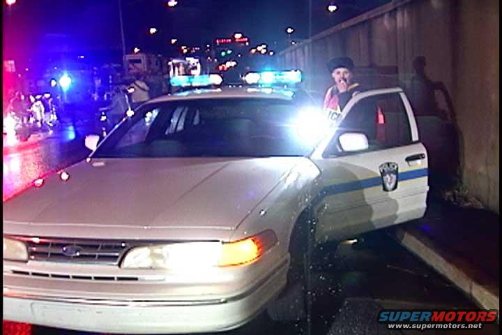 Police car with officer standing by the open door. Lights are flashing