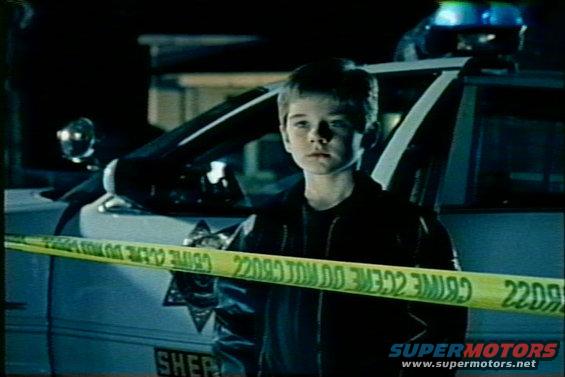 Police car behind crime scene tape with a boy in foreground