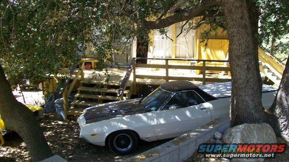 White 1972 Ford Ranchero with black hood stripes parked under trees