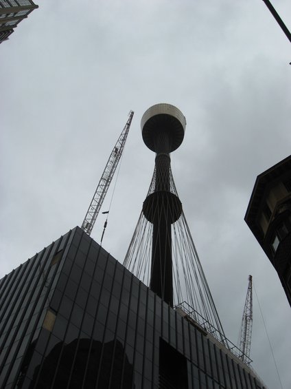Construction site with a tall tower and two cranes against a cloudy sky