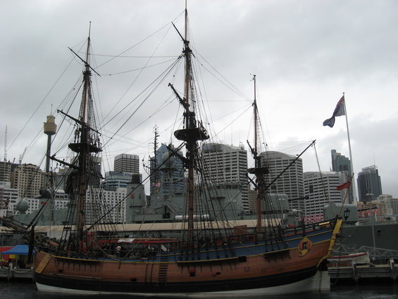 Wooden tall ship with three masts docked in a harbor with modern city buildings in the background