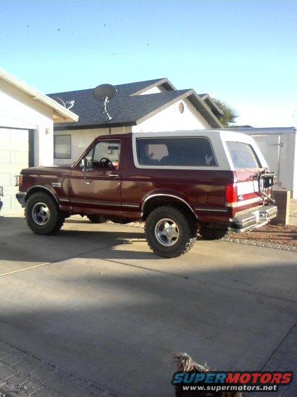 Maroon Ford Bronco with white removable top, side view, lifted suspension, off-road tires