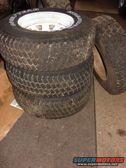 Stack of four Goodyear Wrangler tires, one on a white rim, with visible tread wear