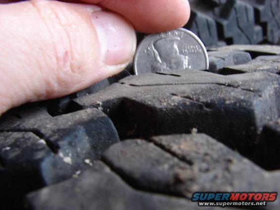 Quarter coin placed in tire tread to show depth