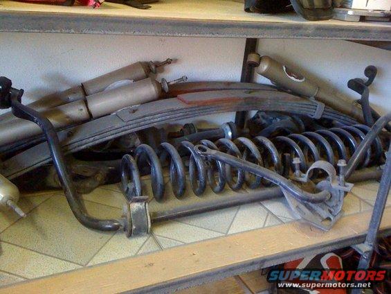 Pile of car suspension parts including shocks, leaf springs, and coil springs