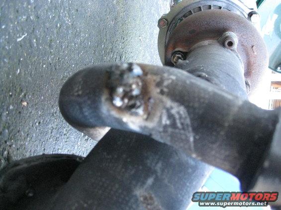 Exhaust pipe with visible weld damage and a bolted flange. The ground is visible in the background