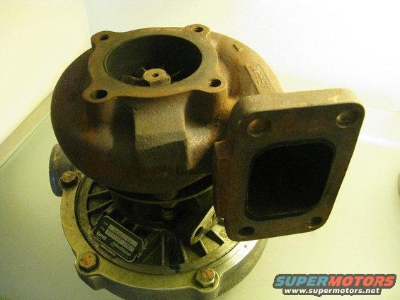Rusty turbocharger with a metal tag attached to its base, showing a black intake and exhaust flange