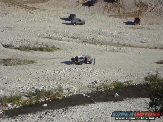 Several off-road vehicles in a dry riverbed with a small stream