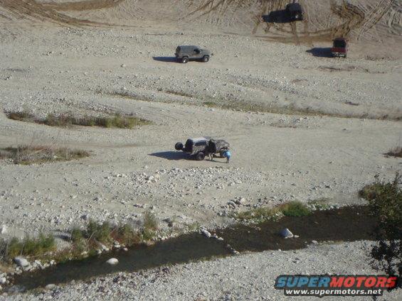 Four-wheel drive vehicles traversing a rocky, dry landscape with a small stream
