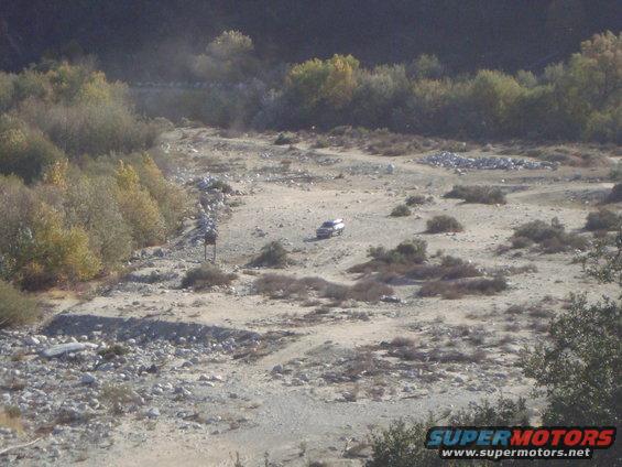SUV in a dry riverbed with brush and trees