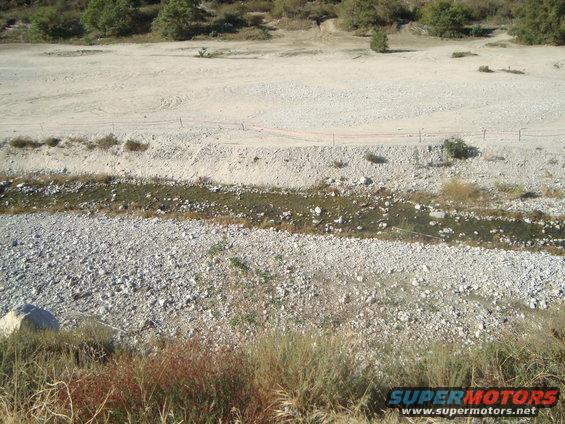 Dry riverbed with sparse vegetation and a dirt road in the distance