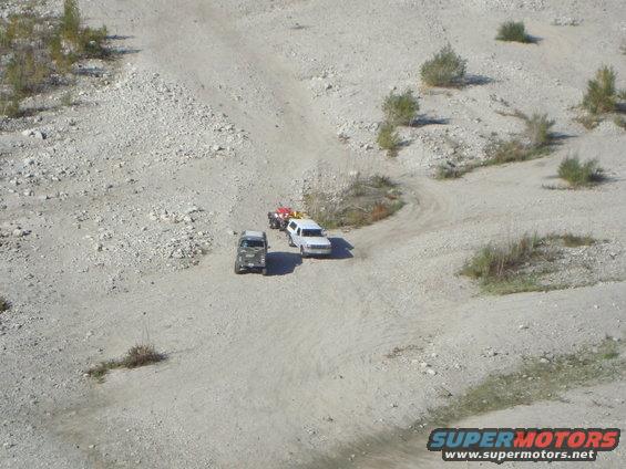 Three off-road vehicles on a dirt track in a quarry