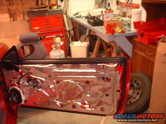 Red car door interior with exposed wiring and speaker, viewed from the inside