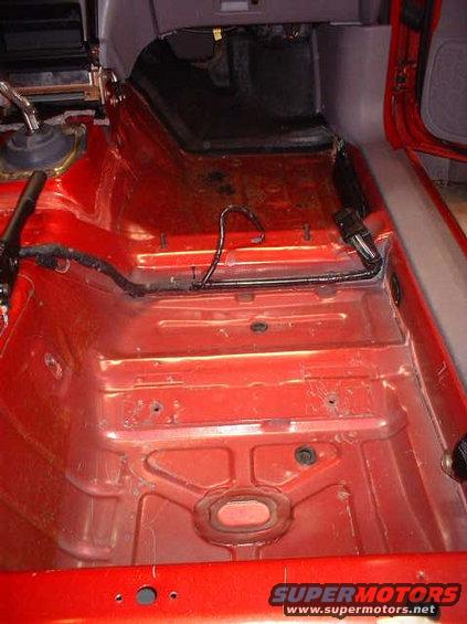 Interior floor pan of a car, stripped down to the metal. Shows red paint and some wiring