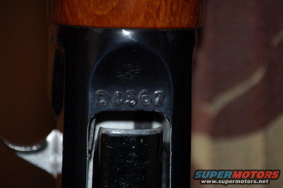 Close-up of serial number D4367 stamped on a dark metal part, with wood grain above
