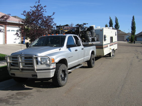 Silver 2005 Dodge 3500 towing a trailer with ATVs on a flatbed
